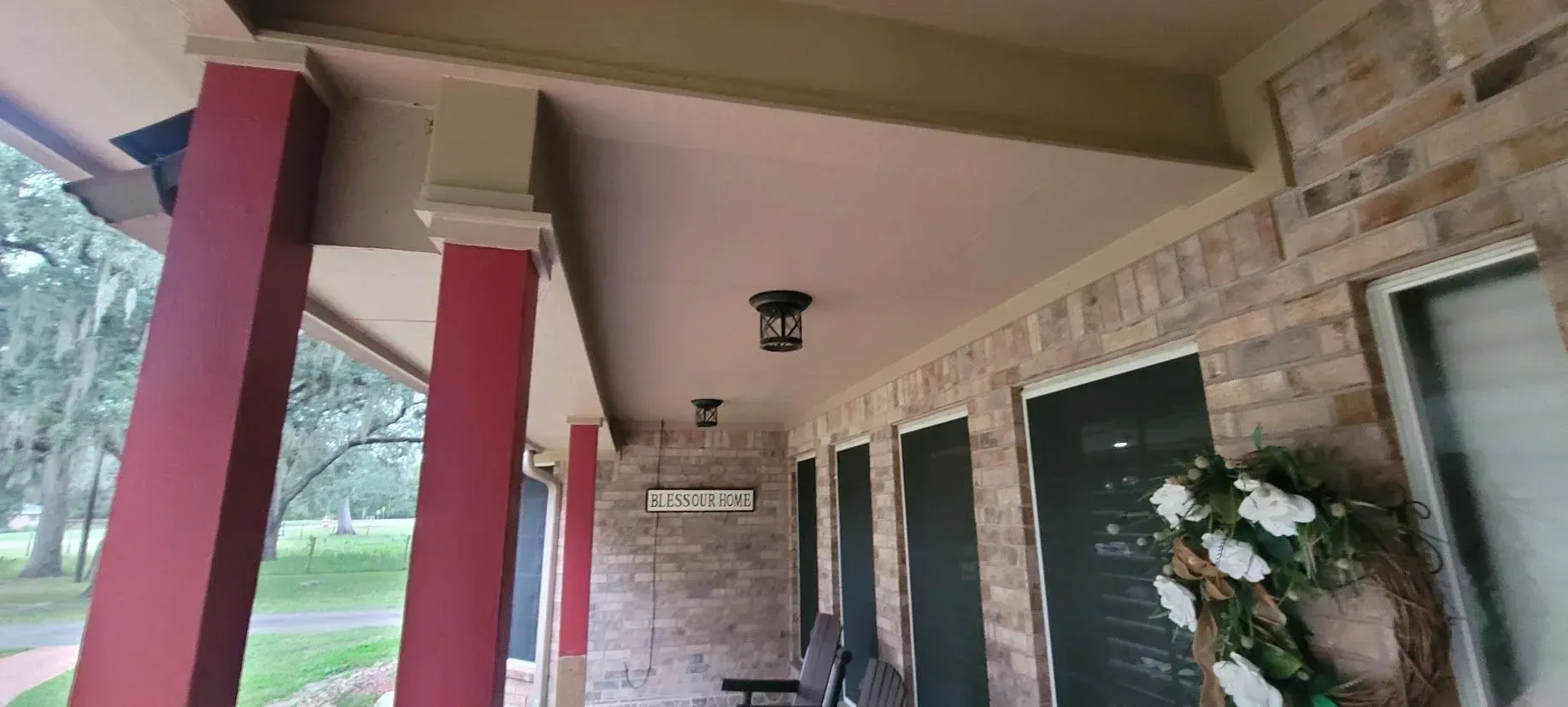 Covered apartment walkway with red columns, stone wall, windows, and potted flowers