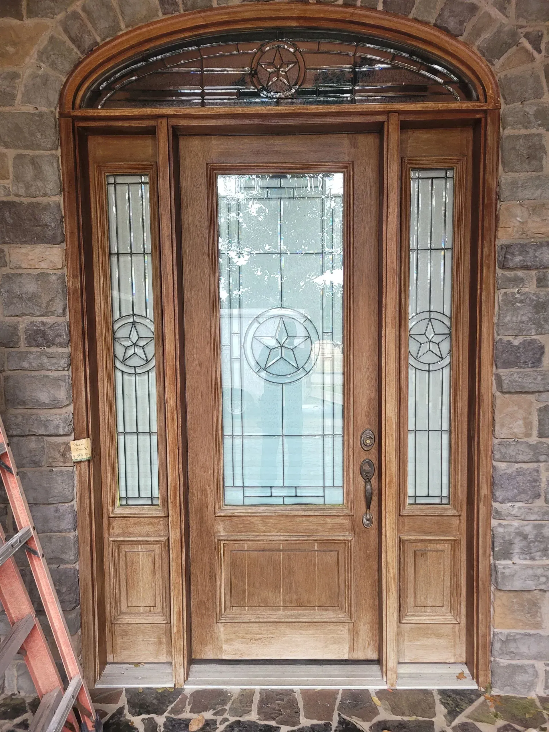 Wooden front door with frosted glass panels and an arched transom, set in a stone wall.
