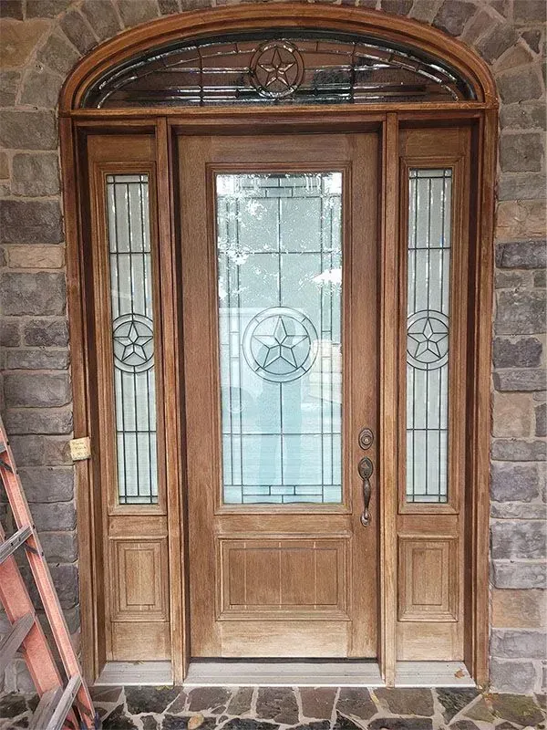 Wooden front door with arched glass panels and sidelights in a stone entryway