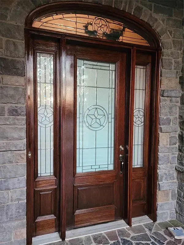 Wooden front door with frosted glass panels and decorative arched transom in a stone entryway