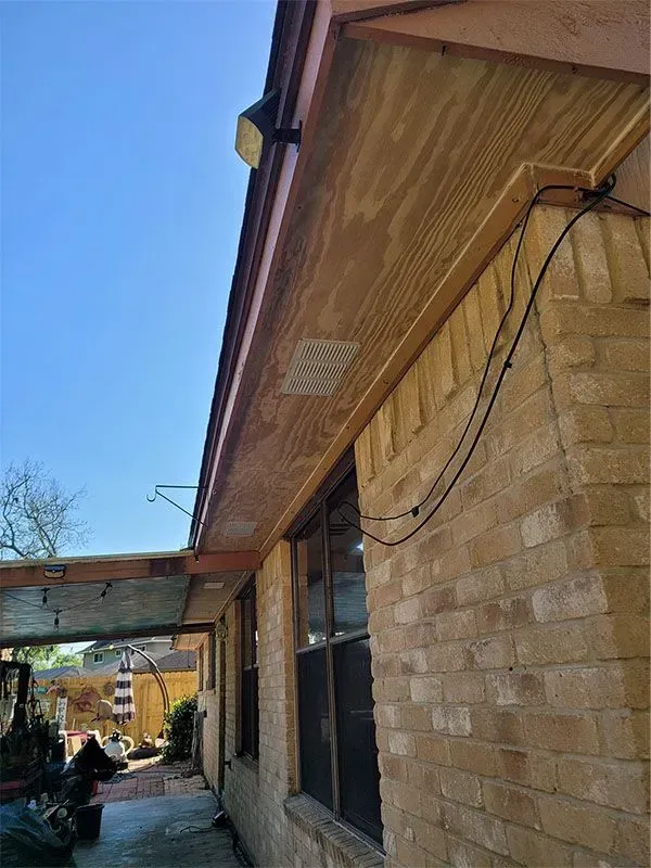 Building exterior with brick wall, wood eaves, and hanging cables under a clear blue sky