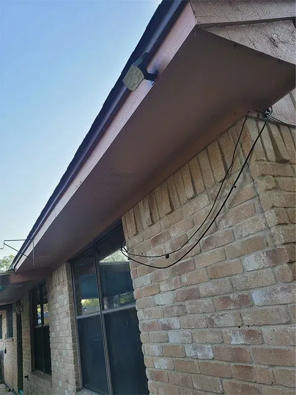 Brick house exterior with a brown roof overhang and hanging cables against a blue sky