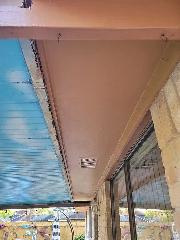 Covered outdoor walkway with a tan ceiling and blue siding, viewed from below