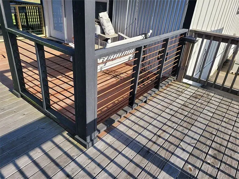 Wooden deck with black railings and a shadow pattern on the floor in bright sunlight