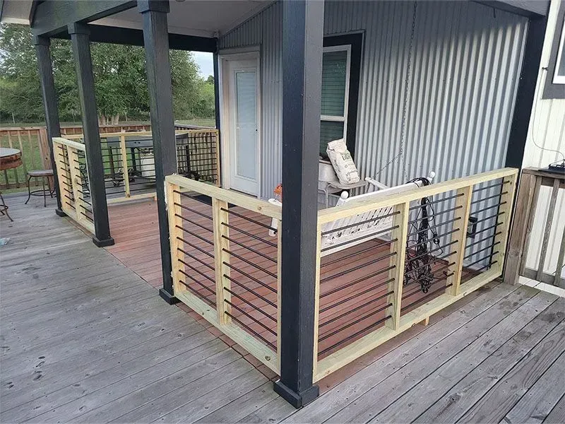 Covered porch with black posts, gray siding, and a small fenced deck area with chairs.