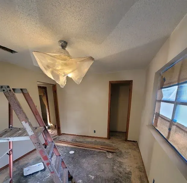 Partially renovated room with ladders, exposed floorboards, and a covered ceiling light