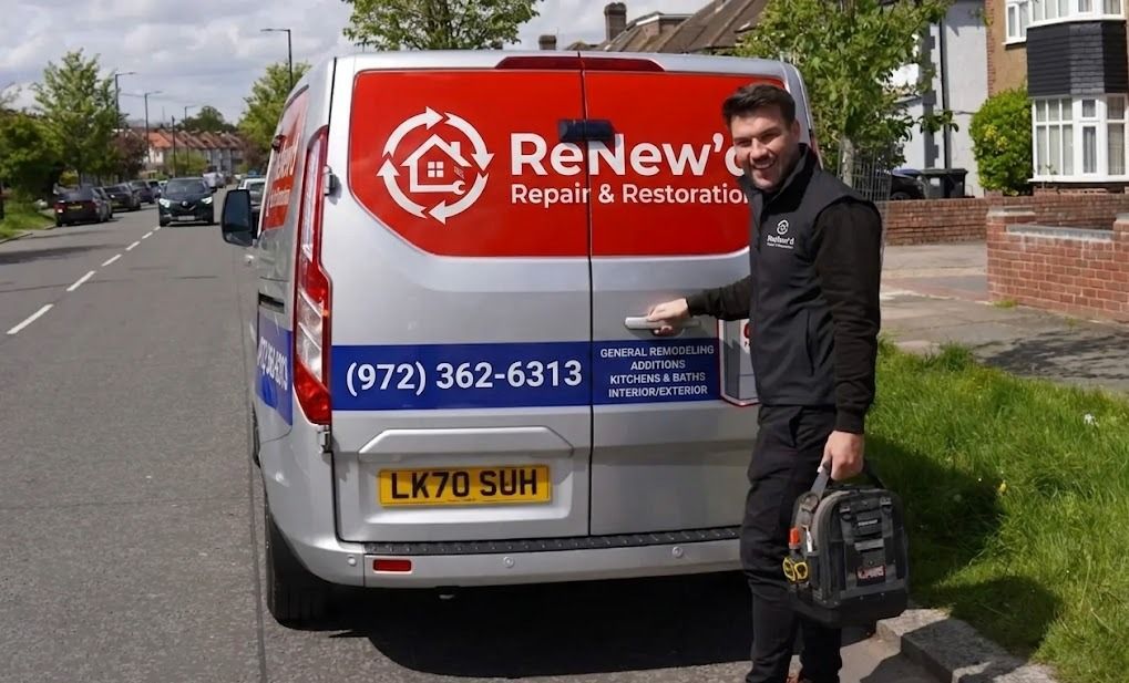 Man standing beside a red Renewal by Andersen van on a residential street, holding tools.