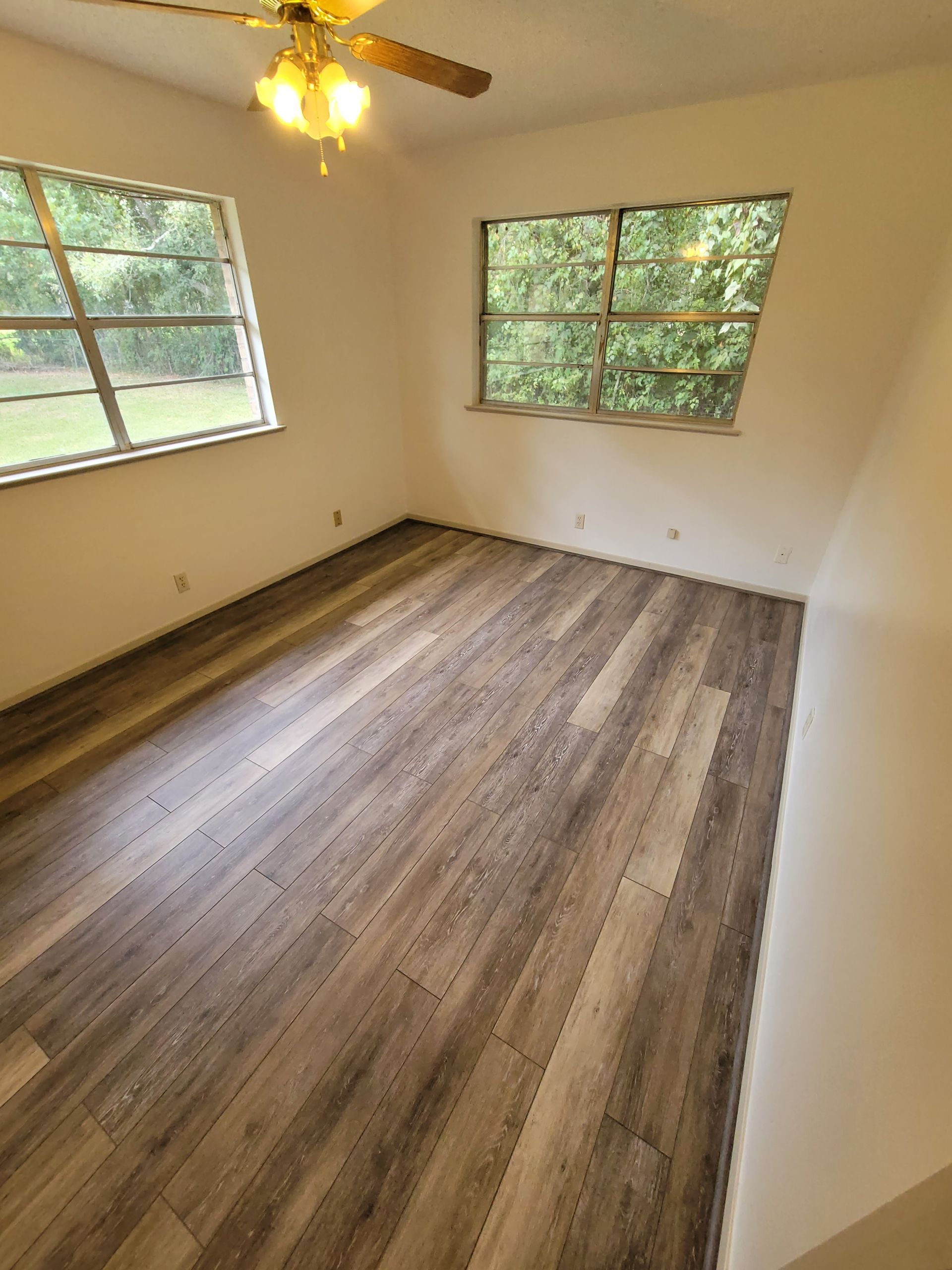 Empty room with wood-look flooring, two windows, and a ceiling fan with lights
