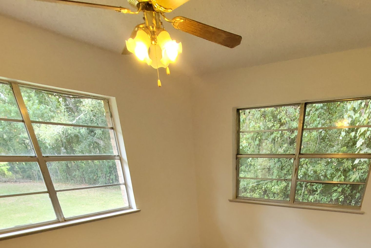 Empty room with beige walls, two windows, and a ceiling fan with lights.