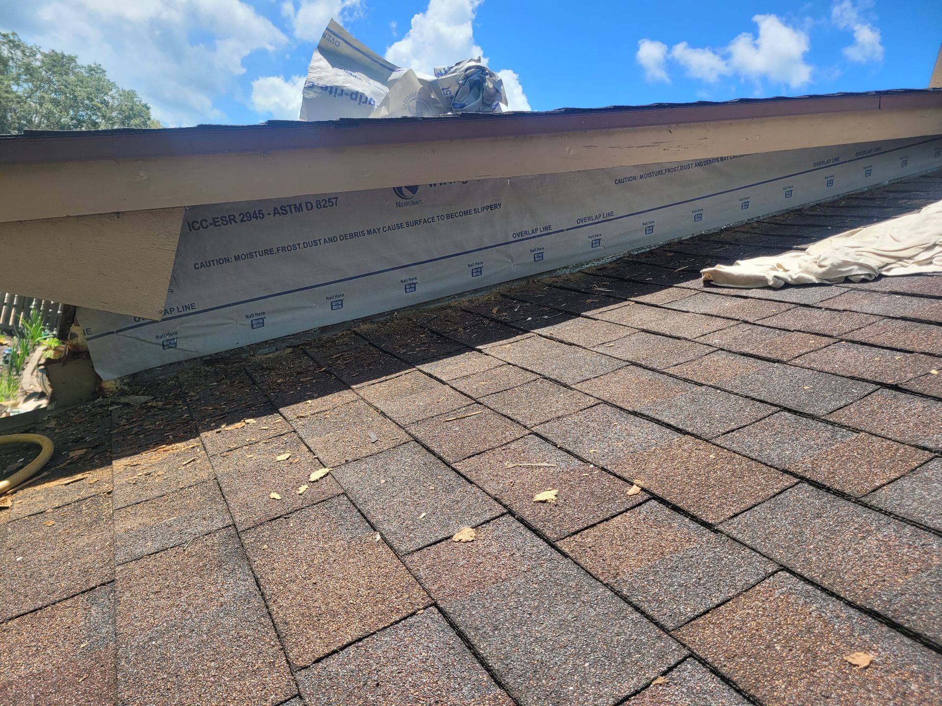 Damaged roof edge with exposed underlayment above brown shingles under a blue sky