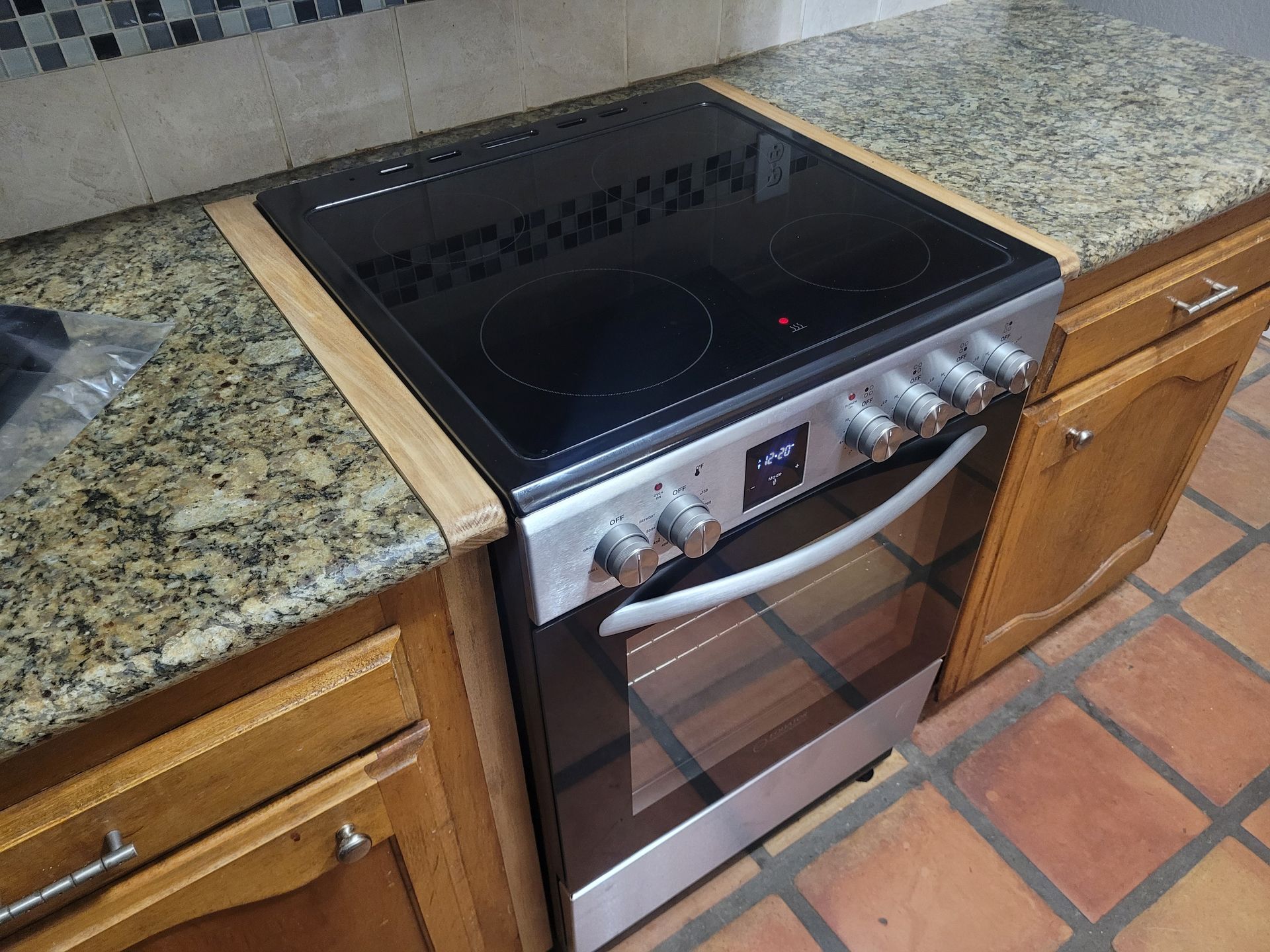 Stainless steel electric range with black glass cooktop and oven, set into a speckled granite kitchen counter.