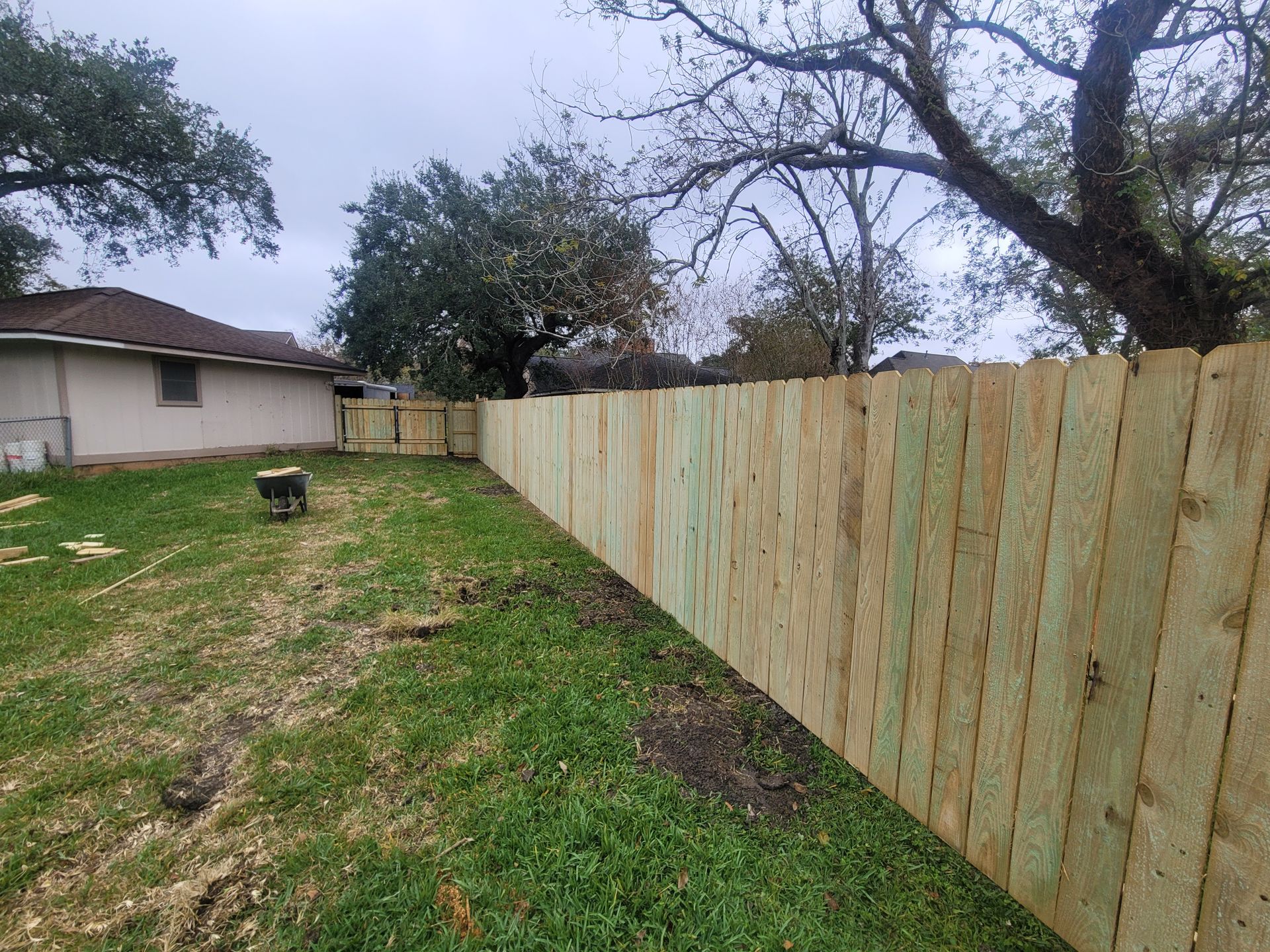 Wooden privacy fence along a grassy yard beside a house under cloudy trees
