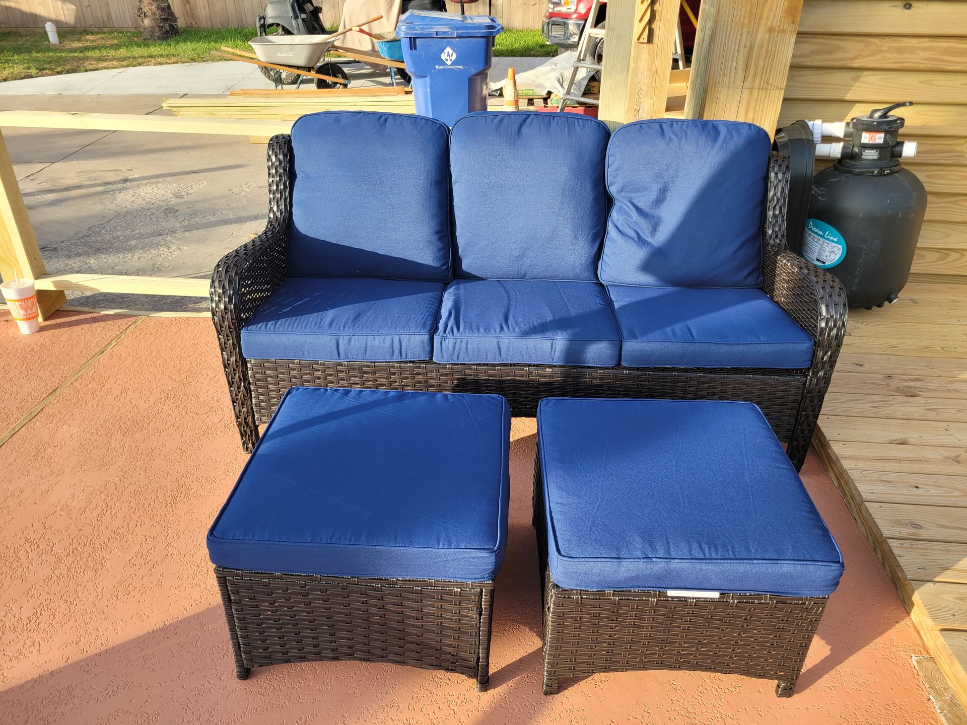 Blue cushioned outdoor sofa set with two matching ottomans on a patio