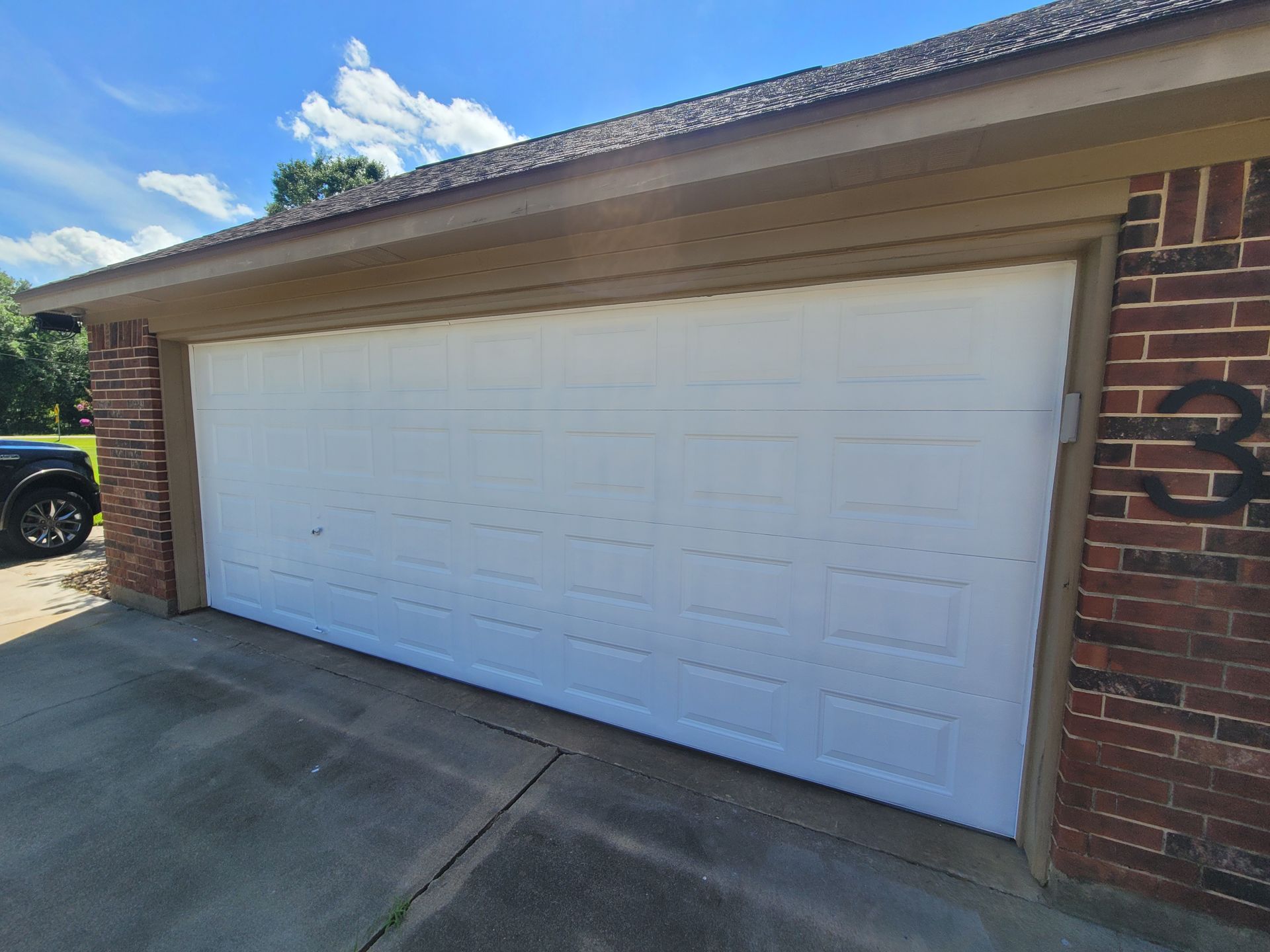 Two-car white garage door on a brick house with a driveway in front.