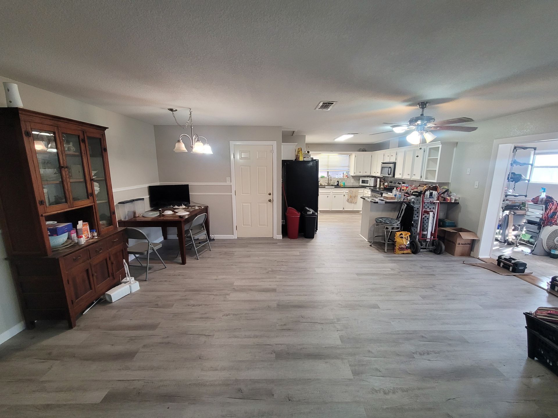 Spacious living room with wood floor, TV, cabinets, kitchen area, and open garage-like space beyond.