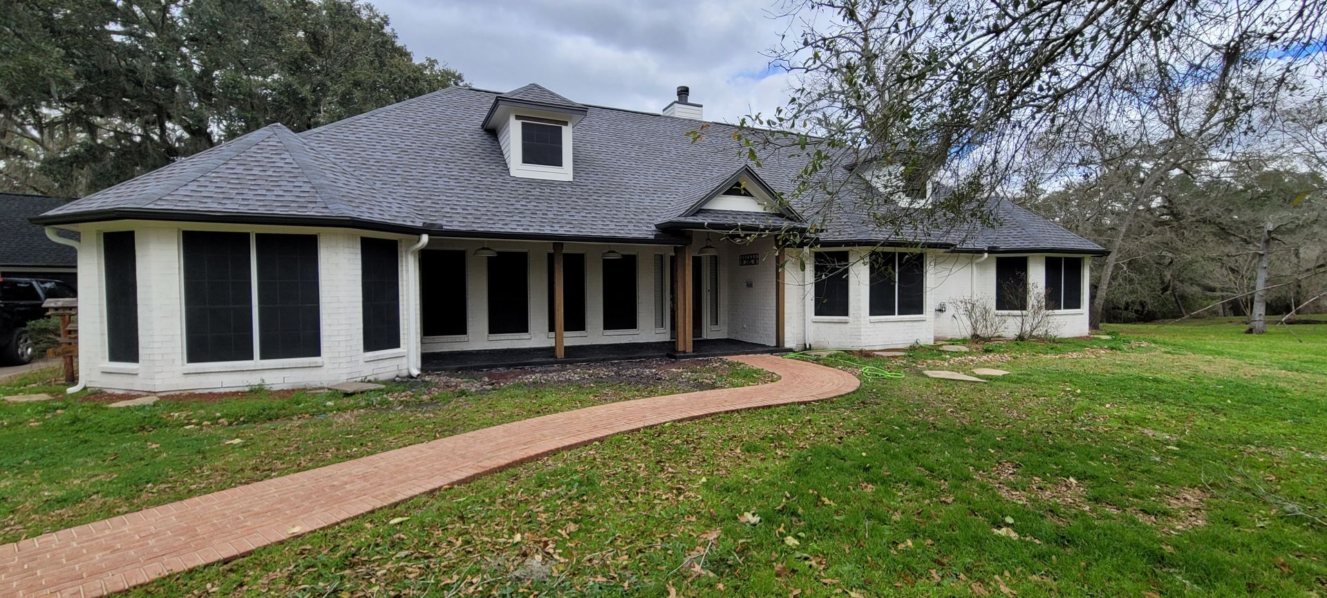 Single-story white house with a dark roof and curved brick walkway in a grassy yard.