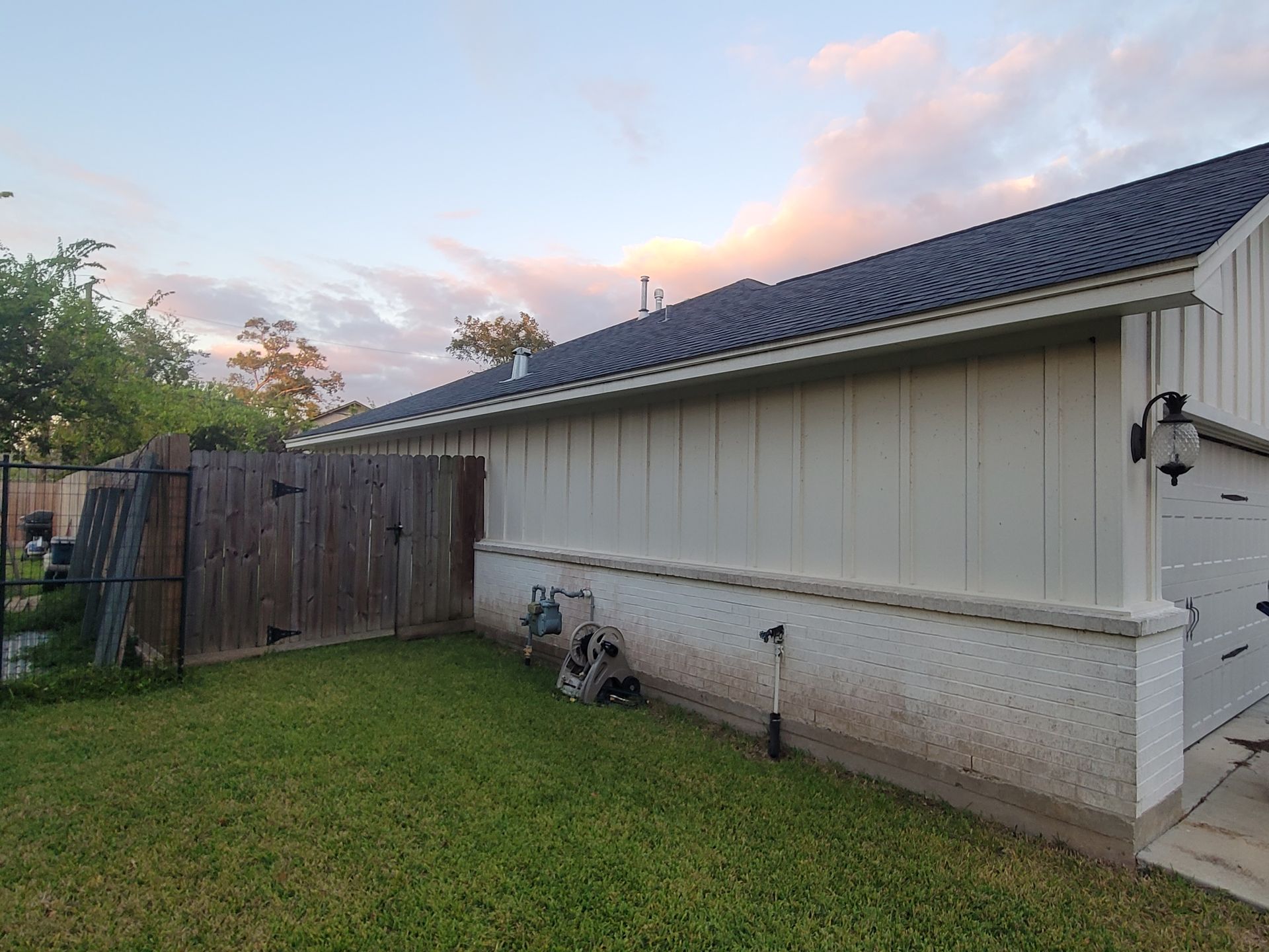 Backyard beside a beige house at sunset, with green lawn, wooden fence, and two bicycles by the wall