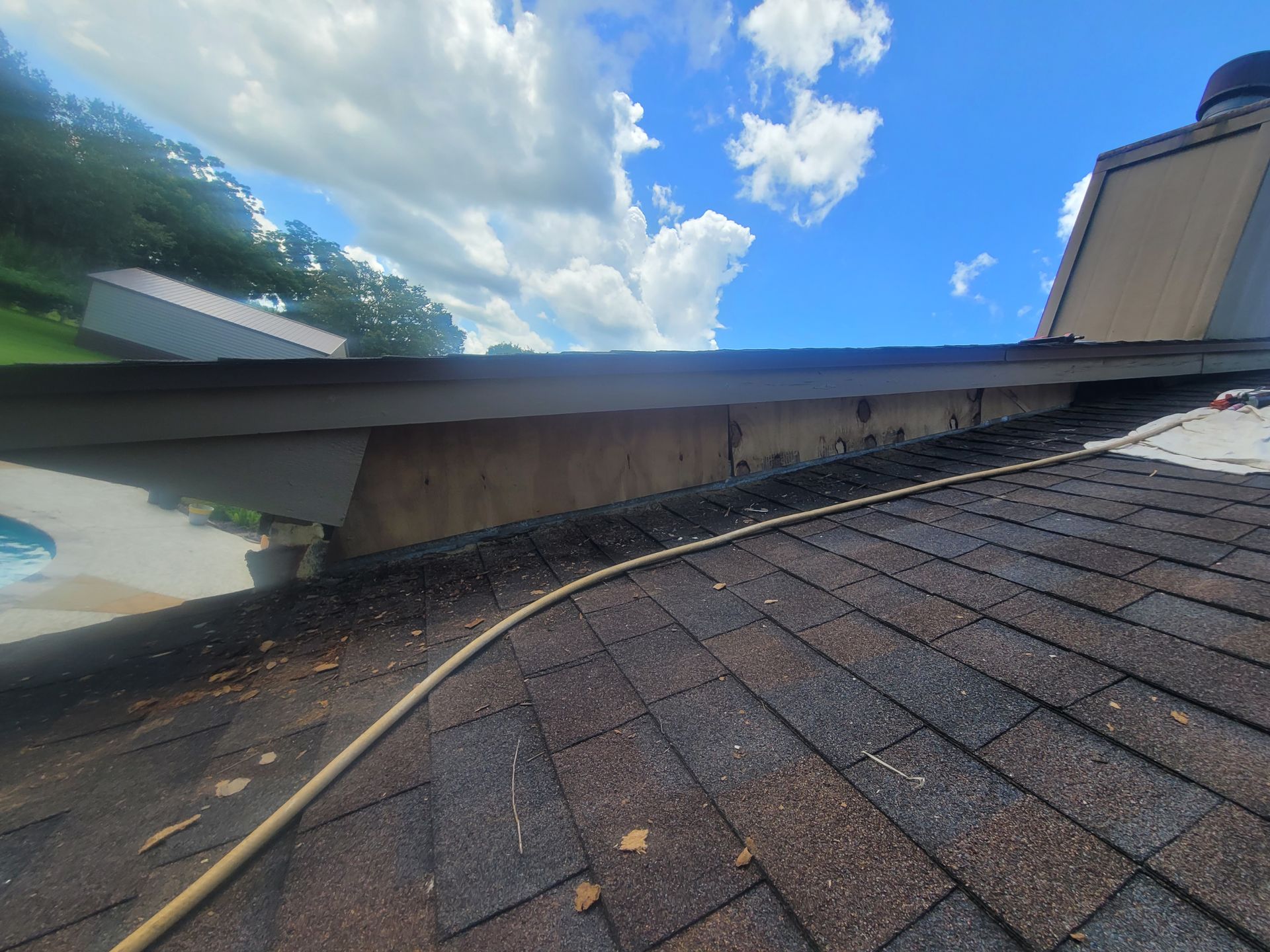 Shingled roof with vent pipe and gutter under blue sky with clouds