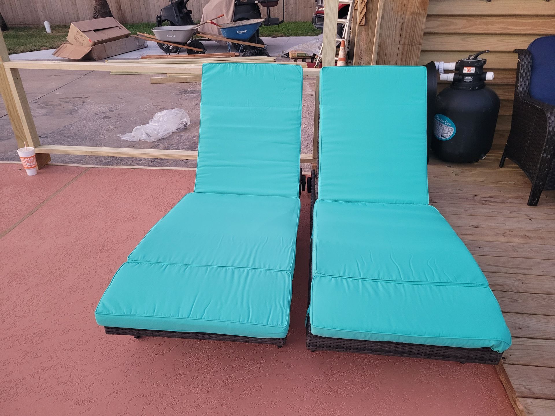 Two turquoise lounge chairs on a patio beside a pool.