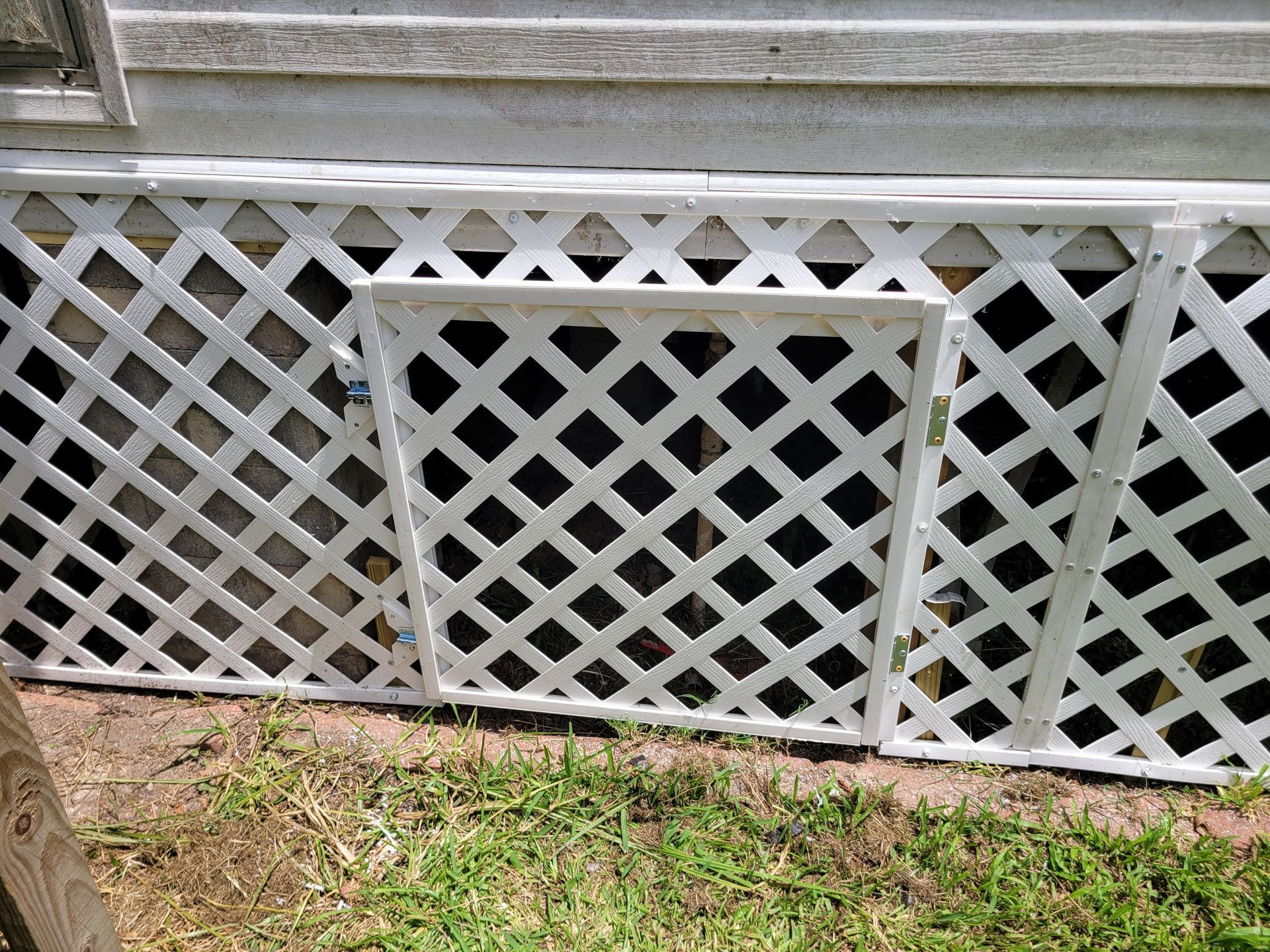 White lattice vent beneath house siding above grass and dirt.