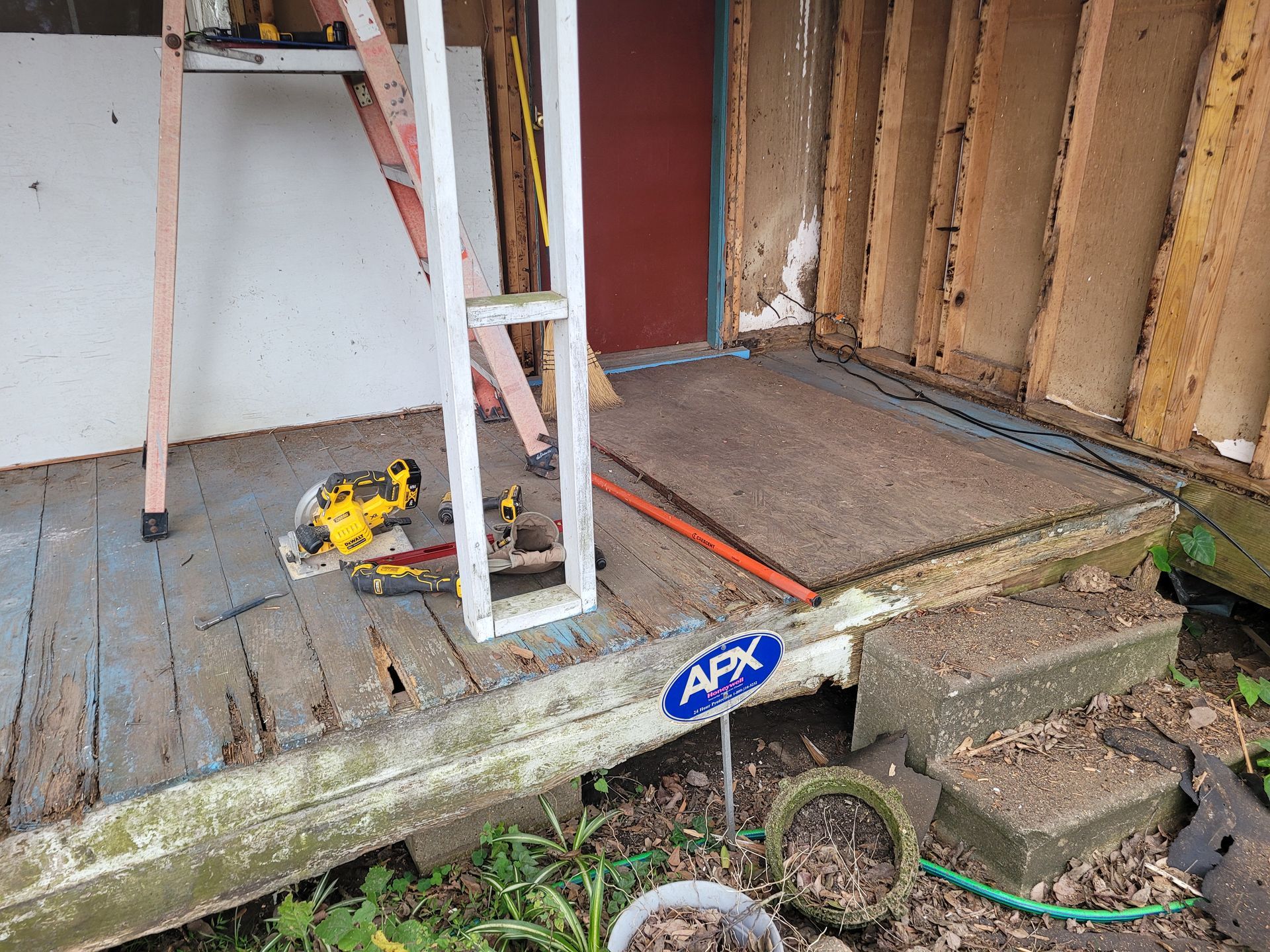 Porch under construction with a ladder, yellow power tool, and exposed wall framing.