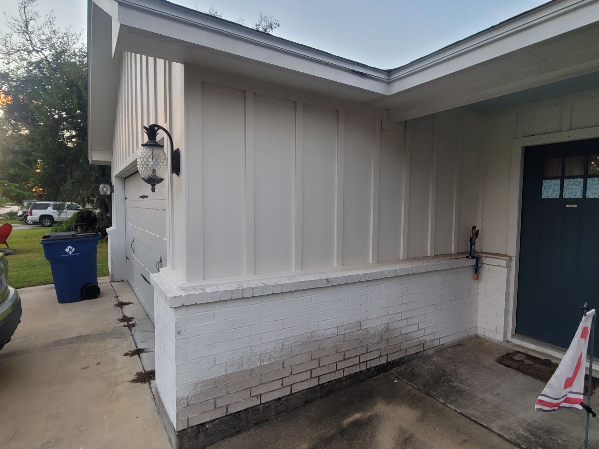 Exterior corner of a white building with blue door, brick lower wall, and wet pavement area