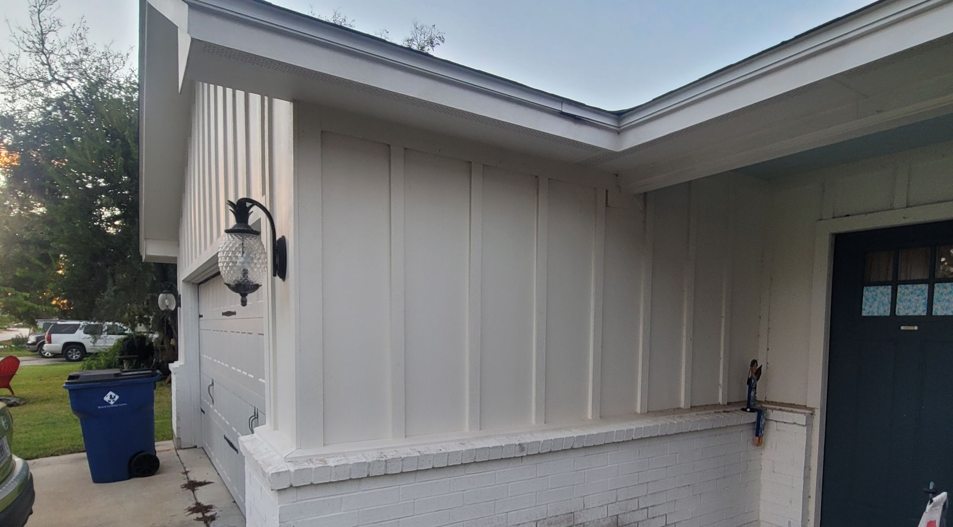 White house exterior with wall-mounted lanterns, dark blue door, and a blue recycling bin nearby