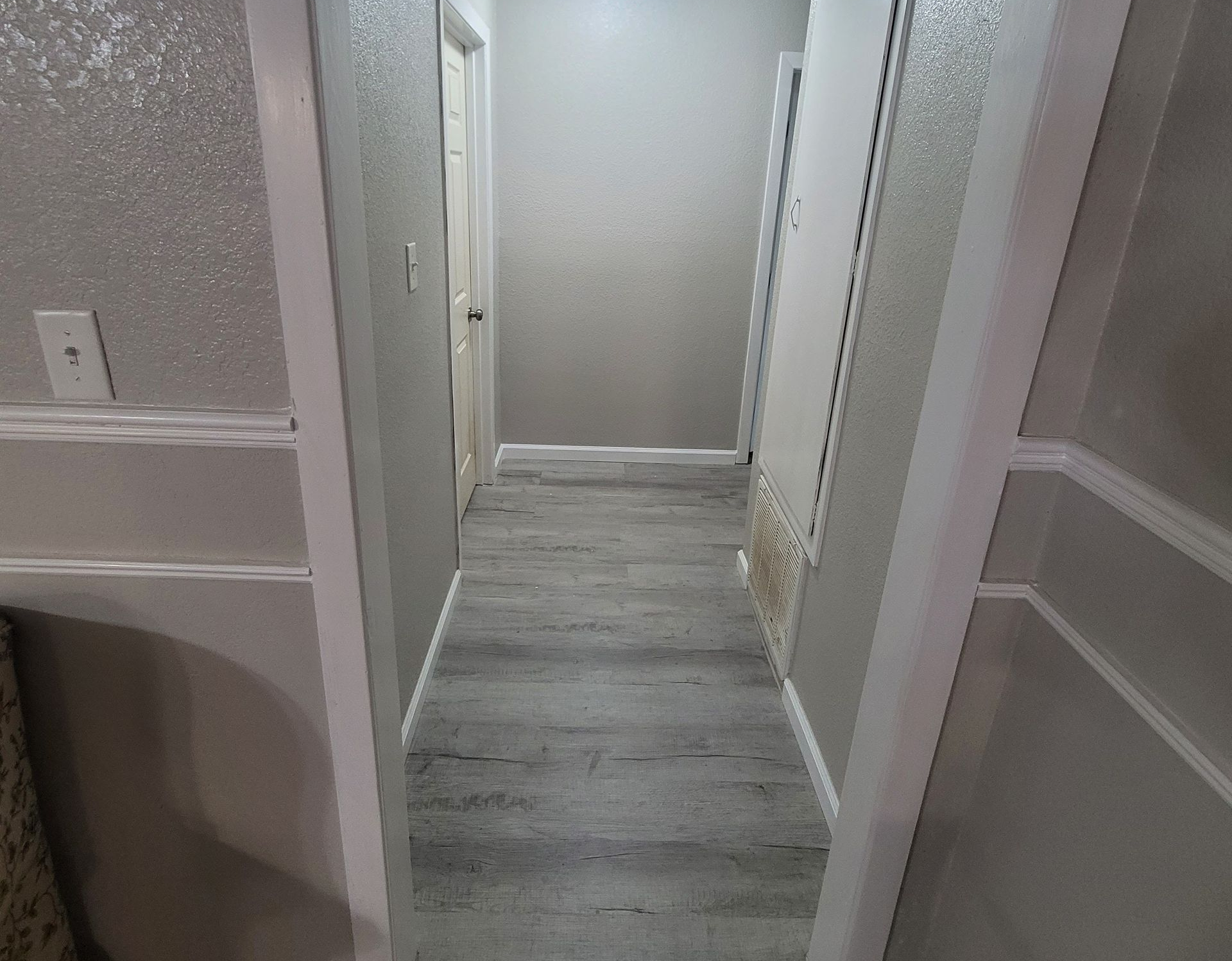 Narrow hallway with white doors and gray flooring, viewed through an open doorway