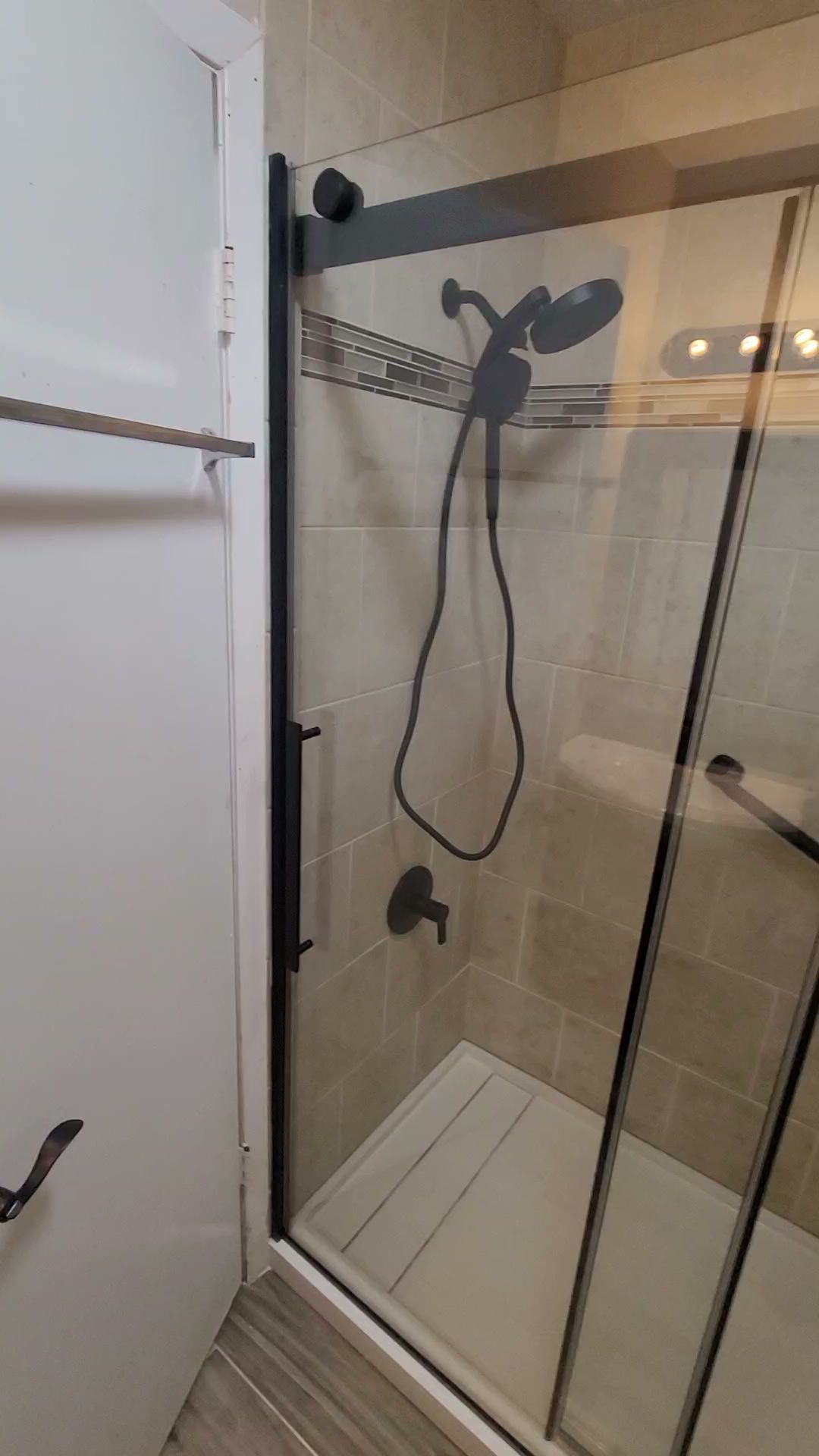 Bathroom shower with clear glass door, wall-mounted showerhead, and white tile walls.