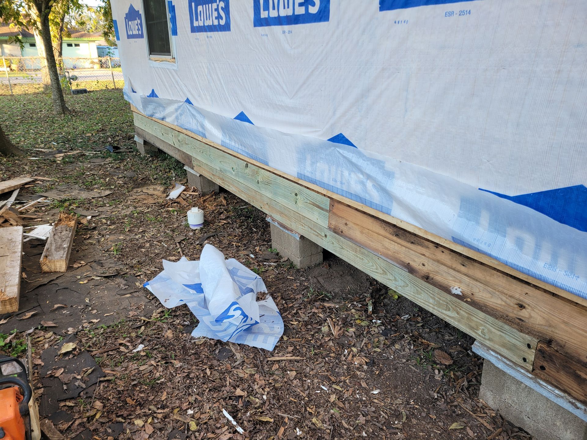 Blue house wrap on a raised wooden structure with a torn sheet on the ground and dirt underneath
