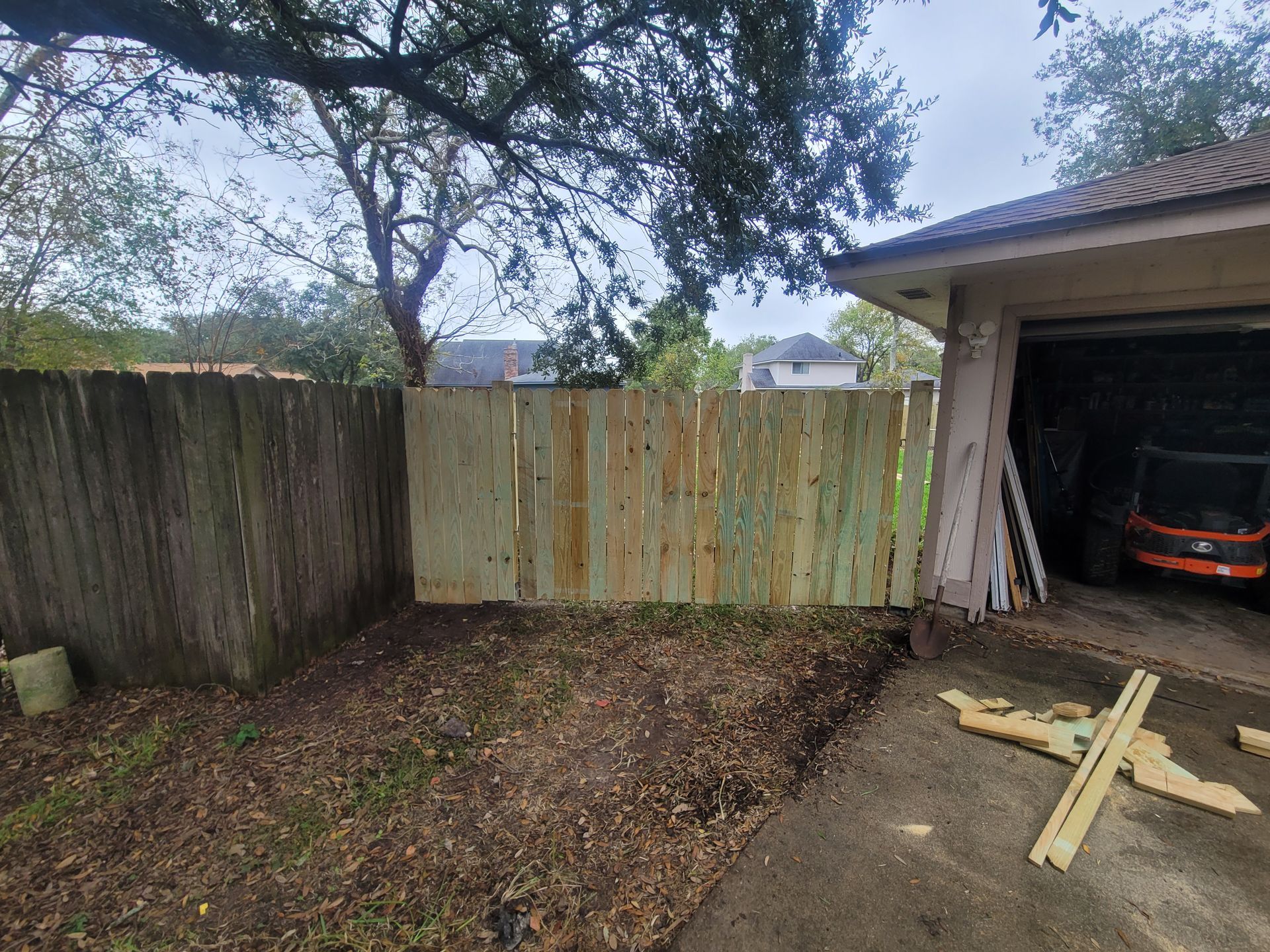 Small backyard with weathered wooden fence, tree overhead, and garage opening on the right.