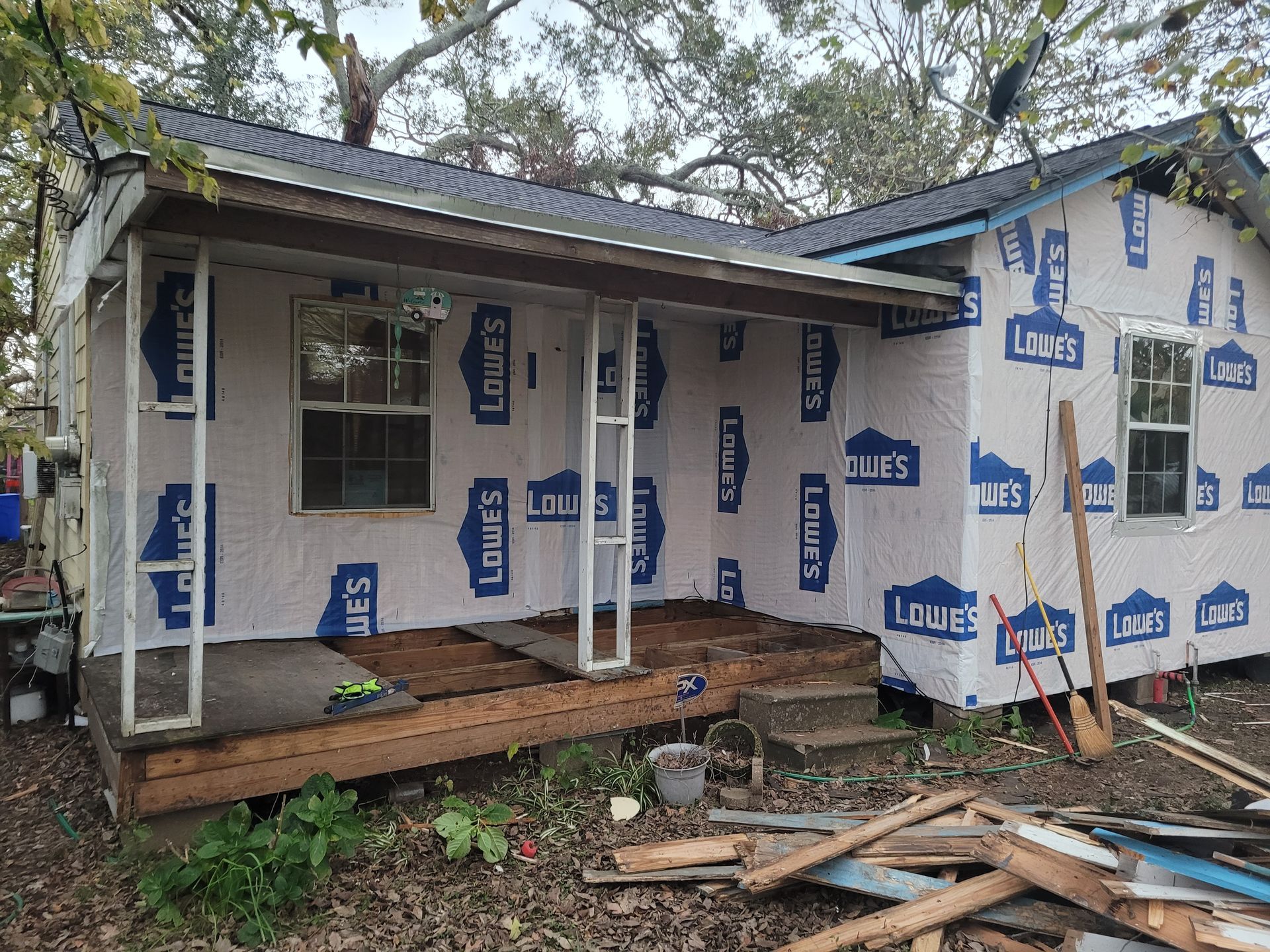 Small house under renovation, wrapped in house wrap with exposed porch and scattered building materials.