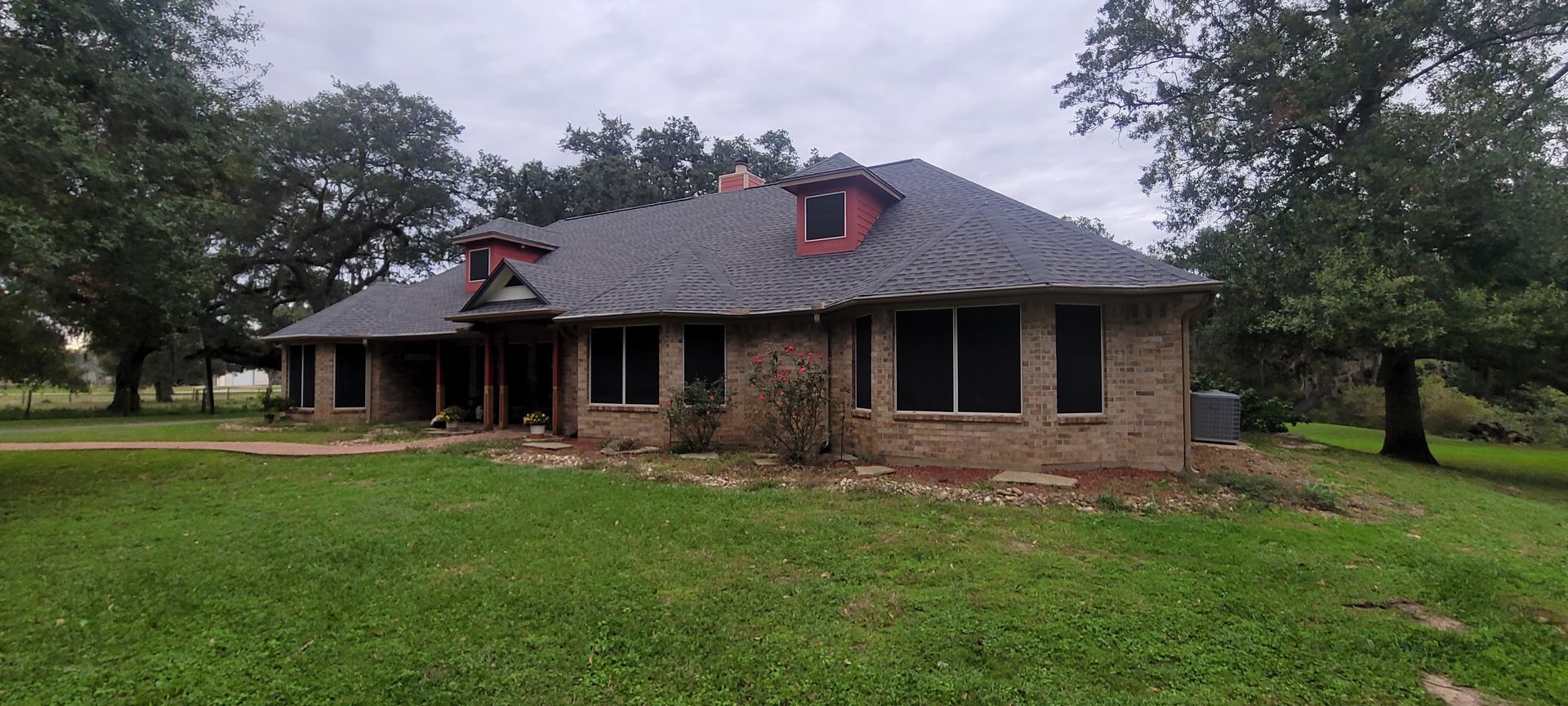 Brick house with dark roof and red dormers, surrounded by trees and a grassy yard