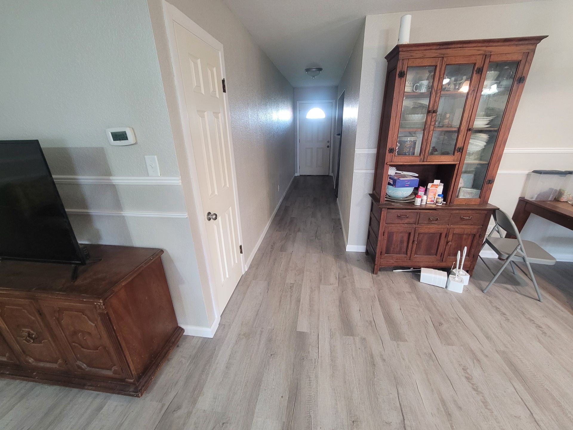 Living room with TV stand, hallway, and wooden display cabinet on light gray flooring