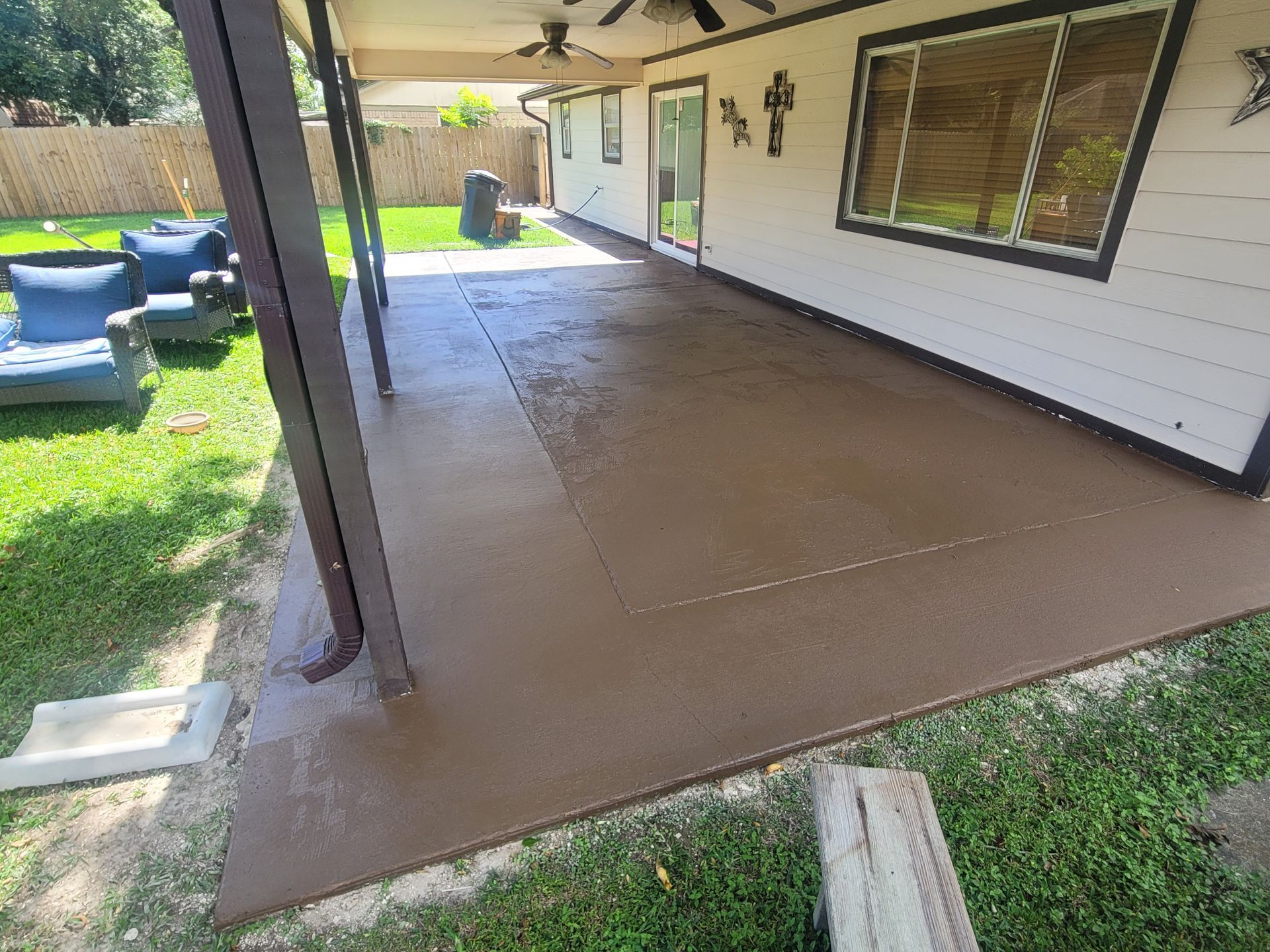 Covered concrete patio beside a house, with a lawn and outdoor seating area.