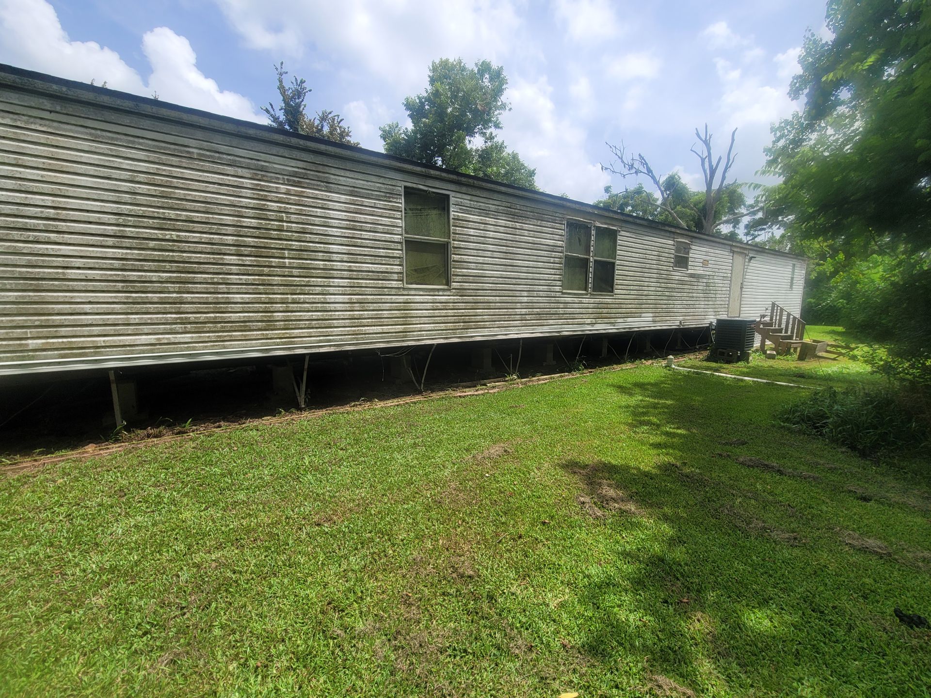 Weathered mobile home beside a grassy yard under a partly cloudy sky.