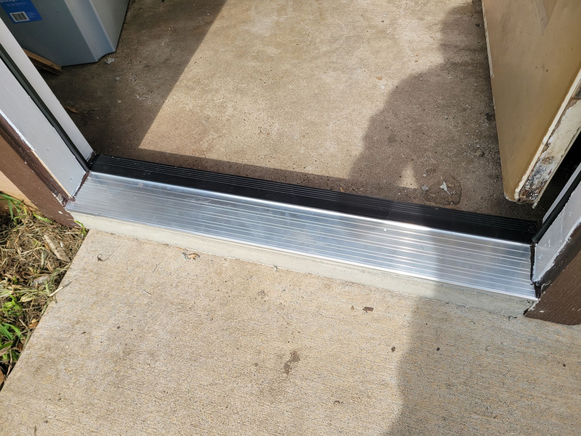Threshold ramp at a doorway, with a metal transition strip from concrete outside to carpet inside.