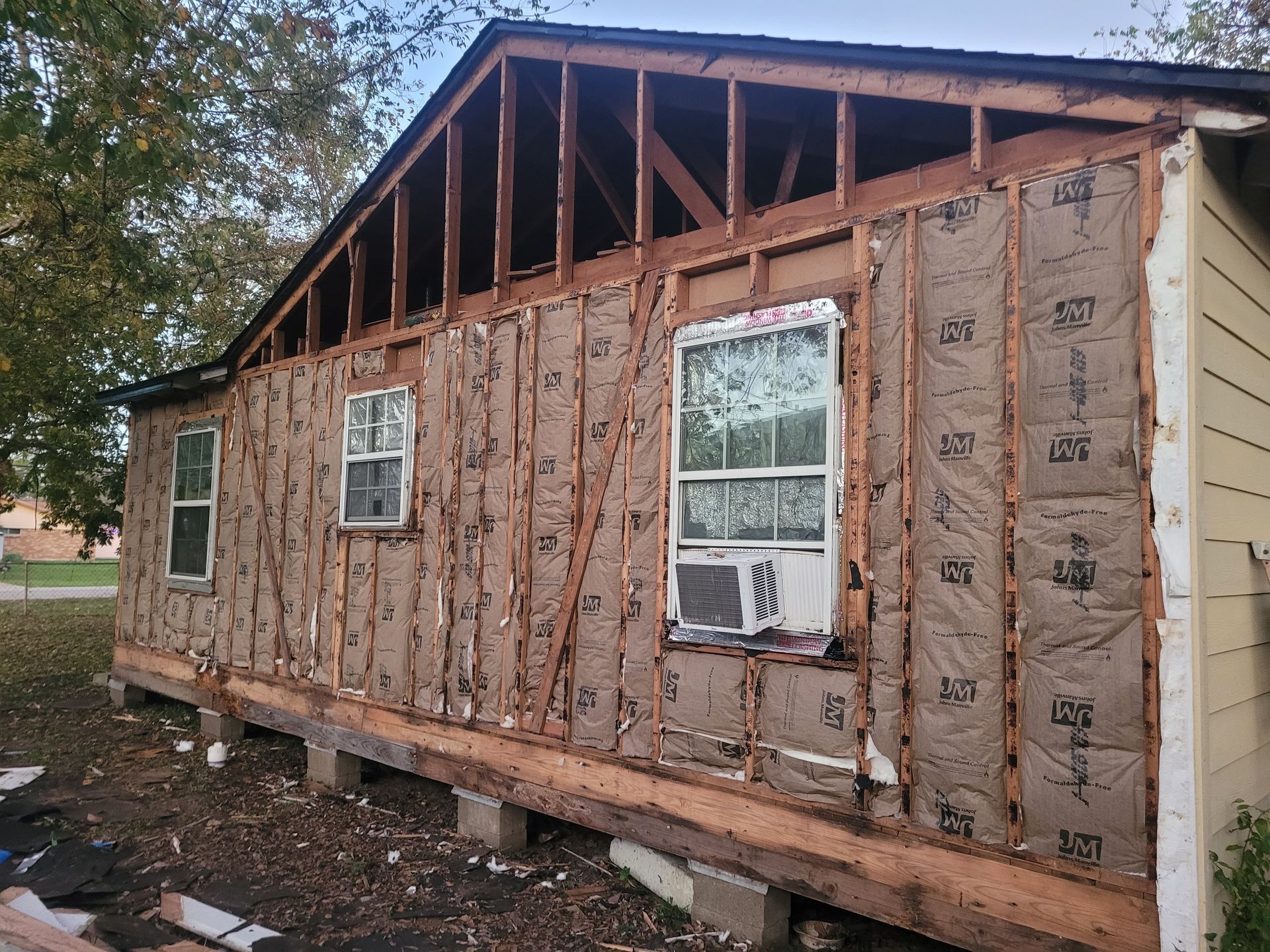 Partially stripped house exterior with exposed insulation and open roof framing under repair
