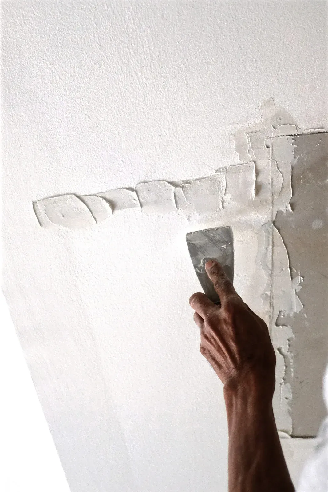 Cracked, peeling wall and ceiling corner with visible water damage and exposed plaster