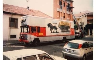 Un camion per traslochi rosso e bianco era parcheggiato in strada, con una scala estesa verso il balcone di un appartamento al secondo piano.