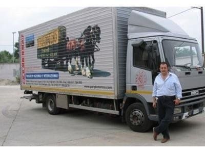 Un uomo si appoggia a un camion per traslochi argentato con la grafica di carrozze trainate da cavalli sul fianco.