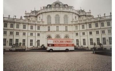 Un furgone bianco per le consegne con insegne arancioni è parcheggiato davanti al Palazzo Stupinigi, un imponente edificio storico di colore chiaro.