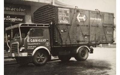 Una vecchia foto in bianco e nero di un camion della Gariglio con un grande container squadrato parcheggiato in una strada cittadina.