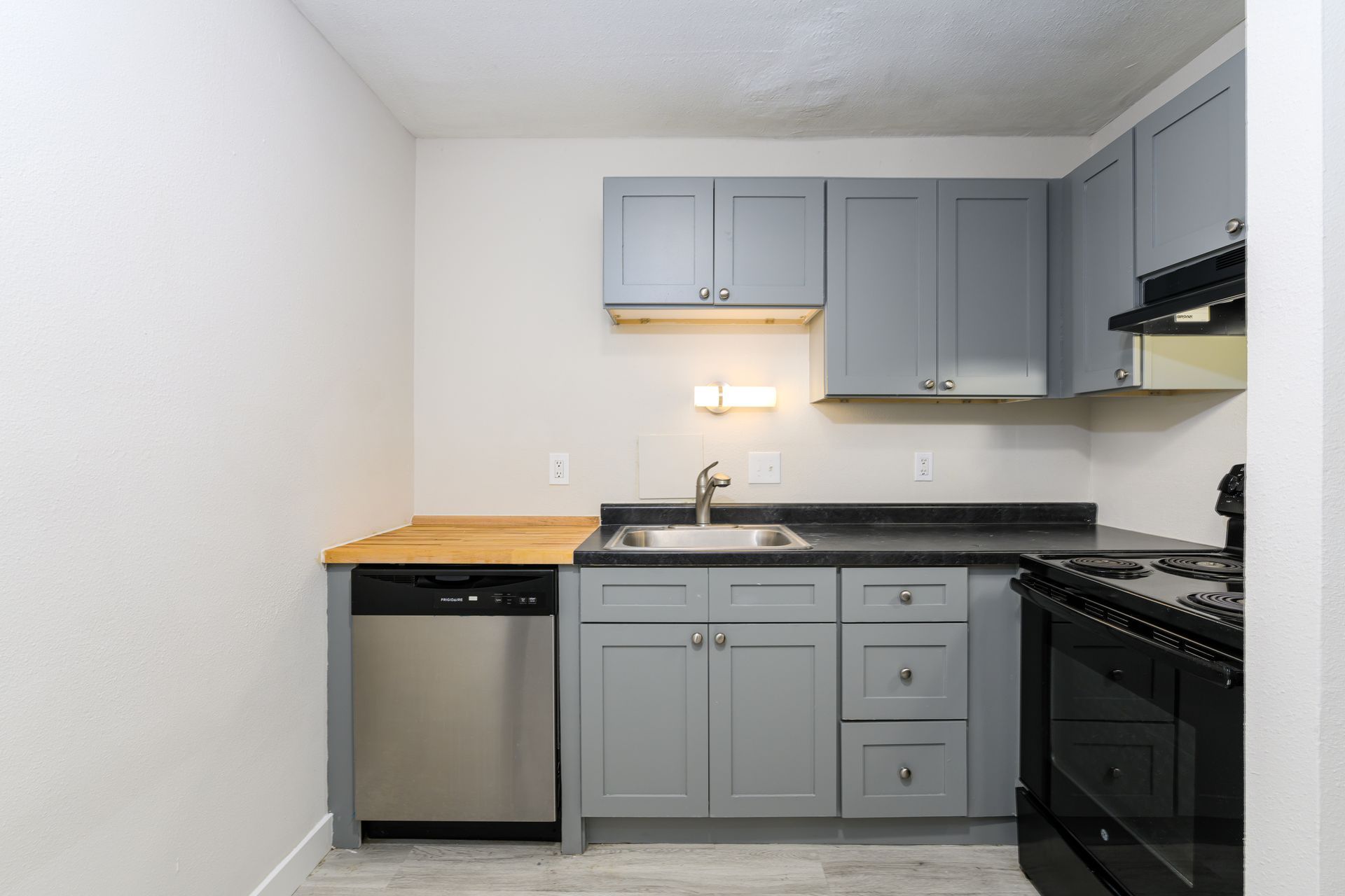 A kitchen with gray cabinets , a black stove , a sink , and a dishwasher.