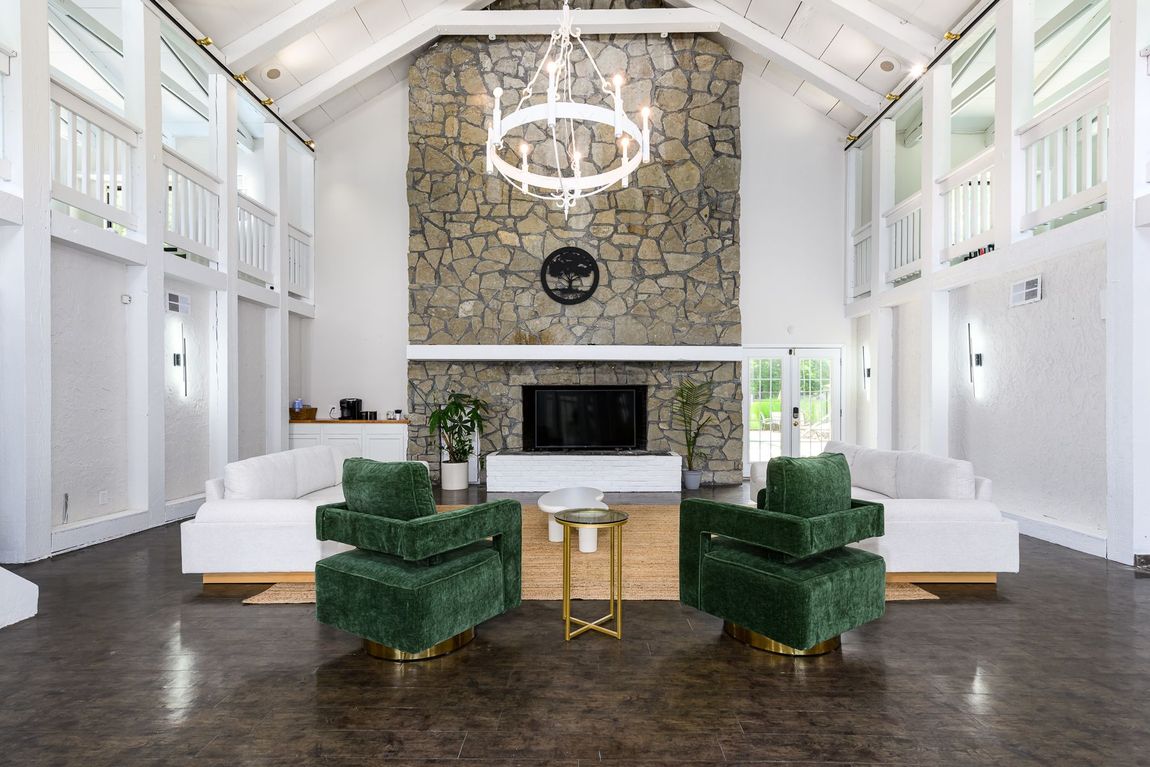 A living room with green chairs , white couches , a fireplace and a chandelier.