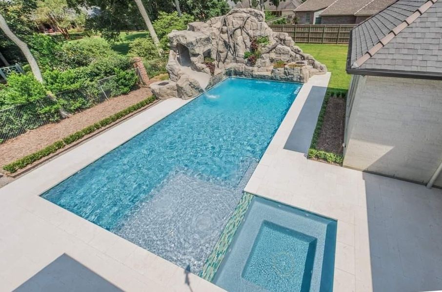 Rectangular pool with waterfall feature, spa, and surrounding concrete patio.