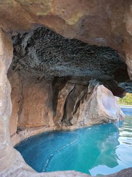 Cave-like structure with blue water; rock formation overhangs the water's edge.