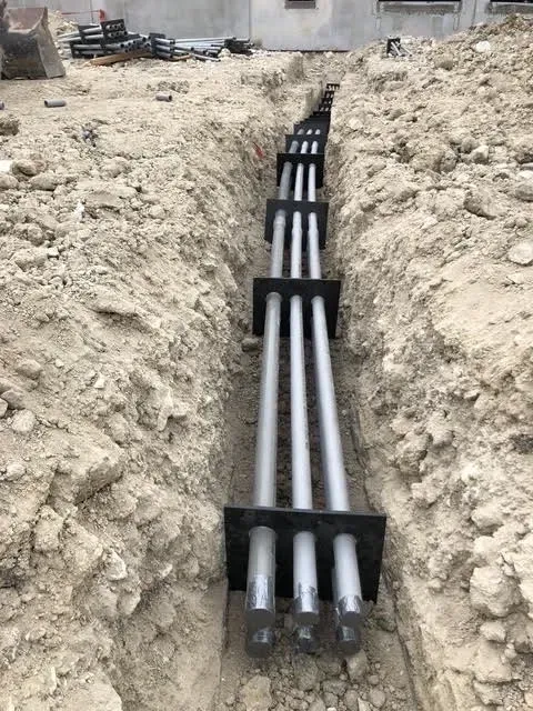 A bunch of pipes are laying in the dirt in a trench.