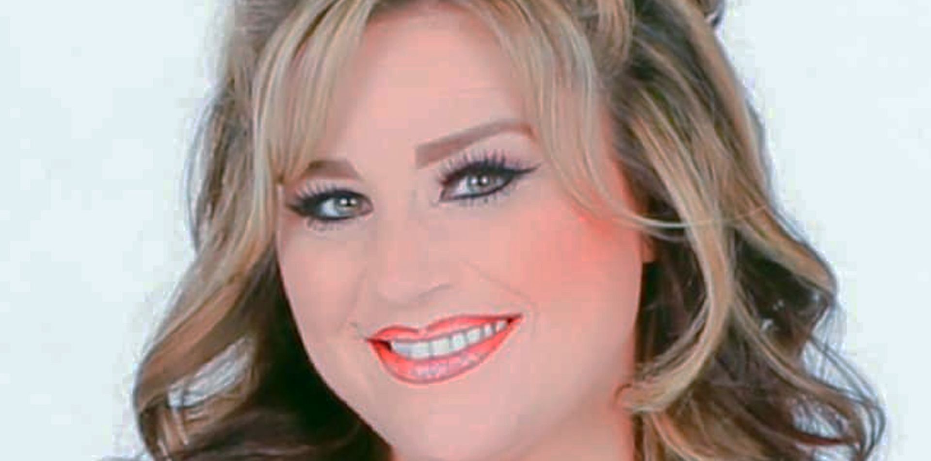 A woman with blonde hair and red lips is smiling for the camera.