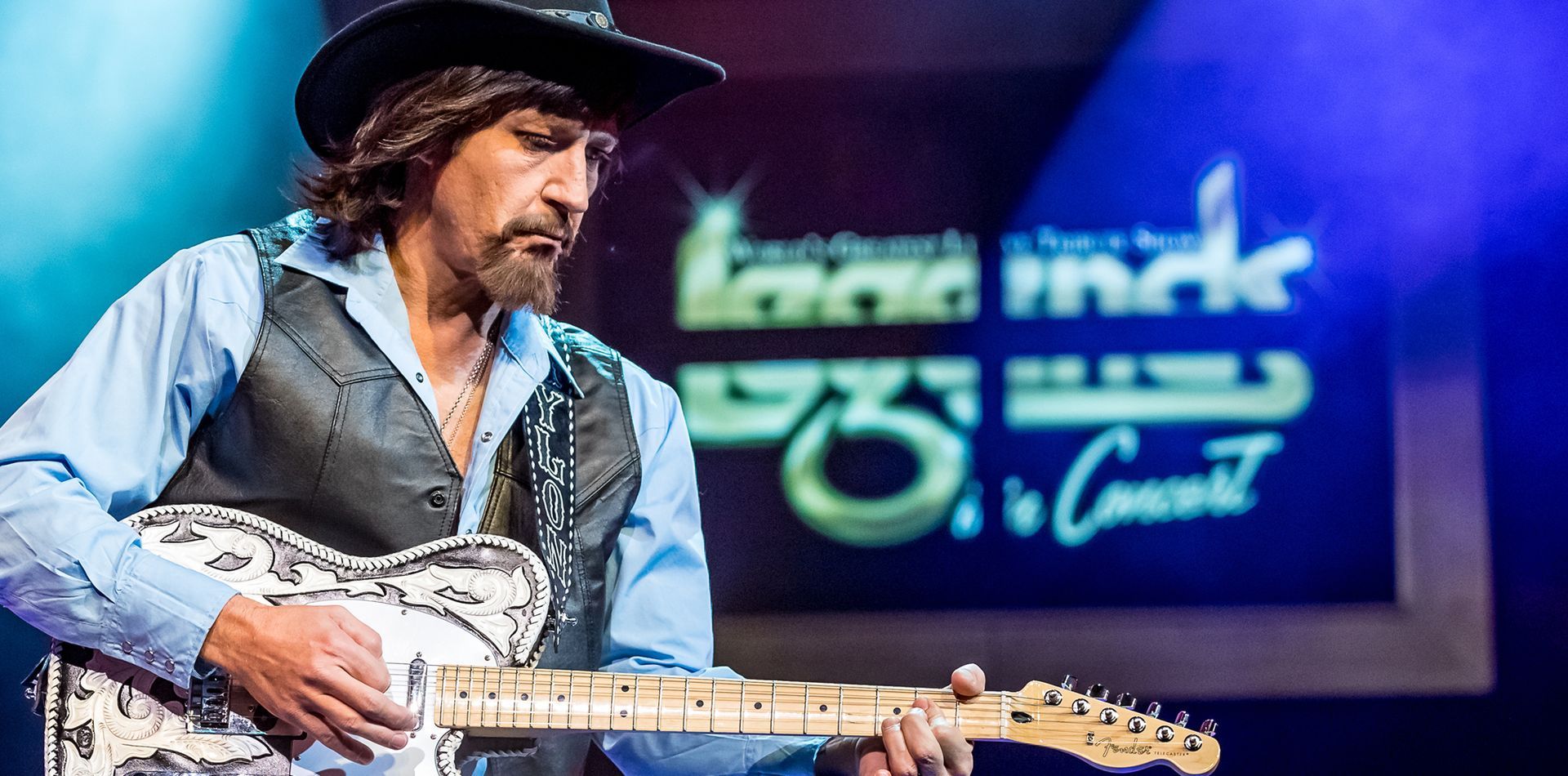A man with long hair is playing a violin on a stage.